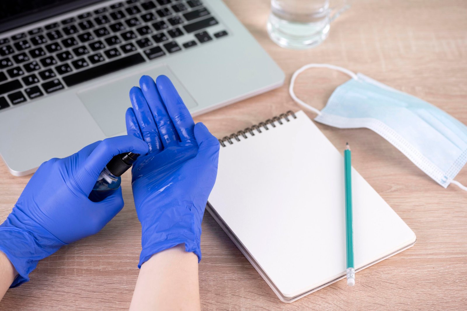 high-angle-hands-with-surgical-gloves-using-hand-sanitizer-desk